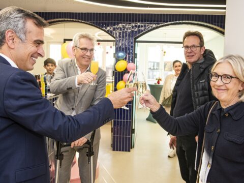 Mehrere Personen stoßen bei der Eröffnungsfeier der Praxis U Smile in fröhlicher Atmosphäre mit Sektgläsern an. Im Hintergrund sind bunte Luftballons und eine moderne Praxiseinrichtung zu sehen.